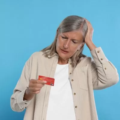 Concerned older woman examining a credit card, appearing confused or worried, possibly about financial fraud or suspicious activity.